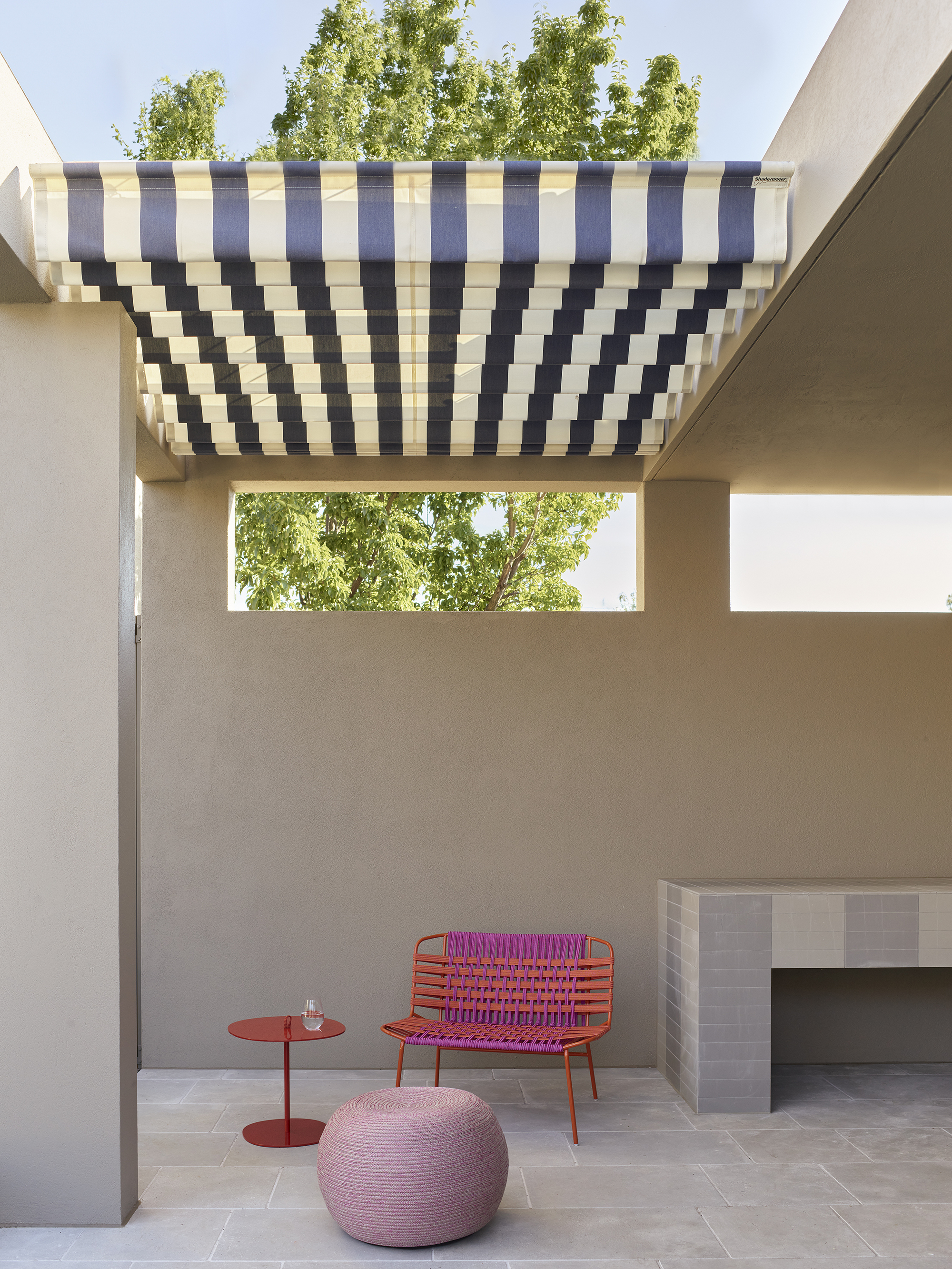 outdoor area with striped retractable pergola with crazy paving, built-in bar, rendered walls, and colorful outdoor furniture