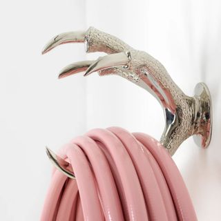 A Garden Glory Claw Hose Holder in silver holding a pink hose