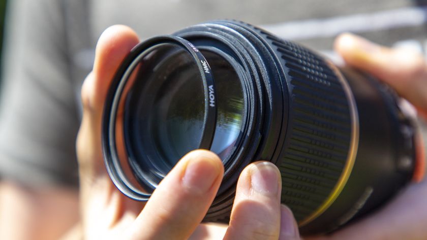 A close-up photo of a Hoya HMC UV filter being attached to the front of a Tamron 90mm f/2.8 macro lens