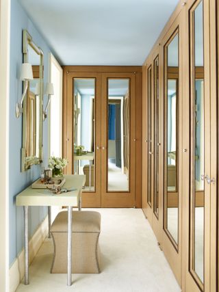 make up vanity in walk in wardrobe with mirrored glass doors, blue walls and cream carpet