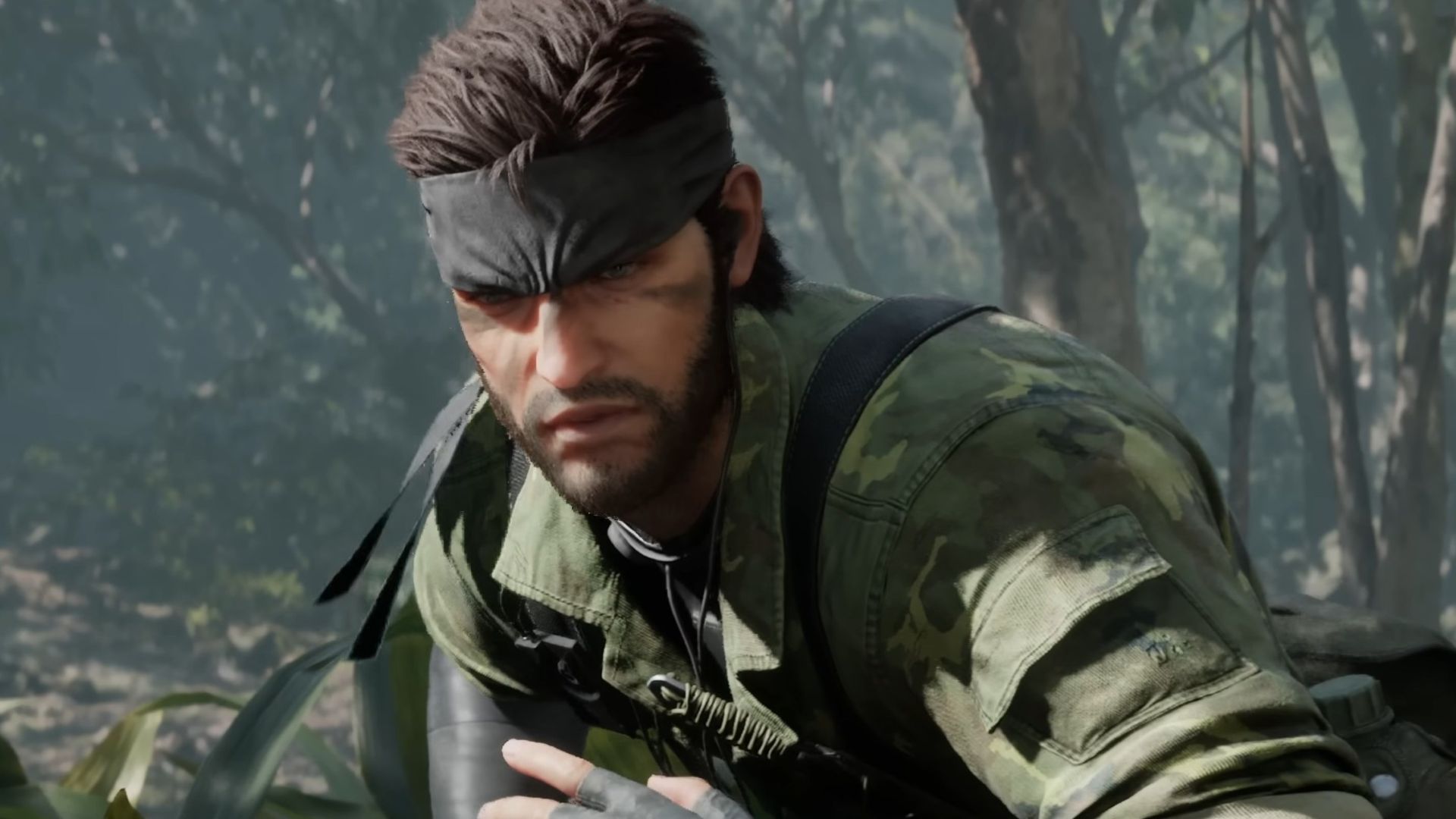 Snake crouching in a forest from the Metal Gear Solid 3 remake. He's wearing camouflage, squinting as he scopes out enemies.