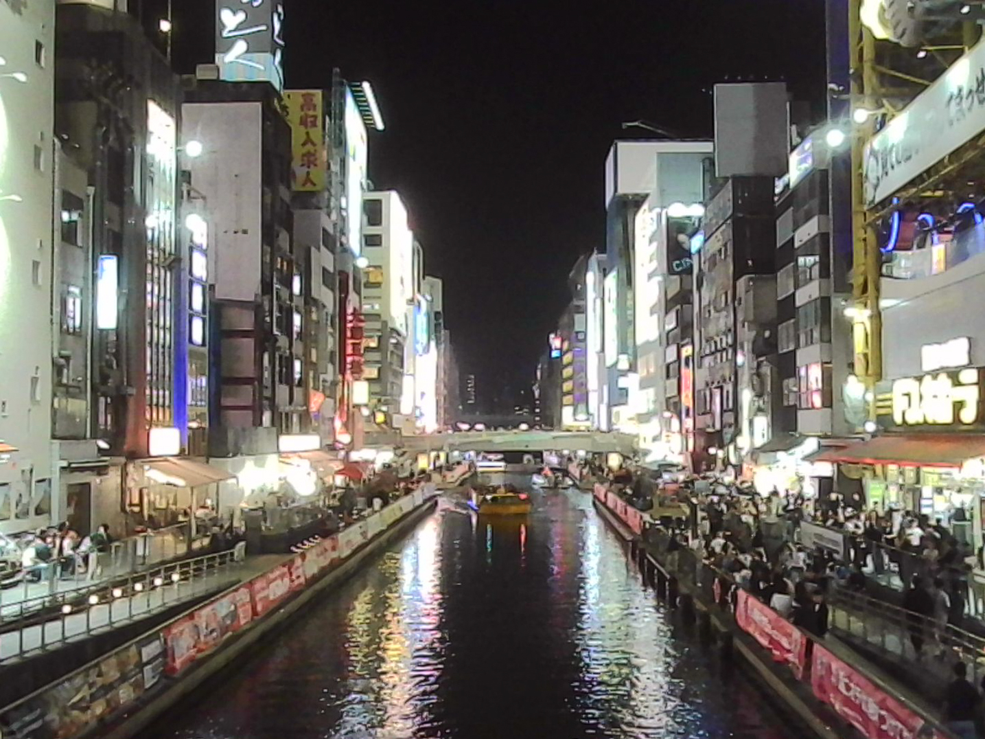 Night view over a canal in Japan with bright city lights reflecting on the water.