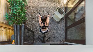 Woman cycling outdoors in back garden following a cycle workout on her laptop