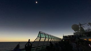people on the deck of a ship look up to see an eclipsed sun.