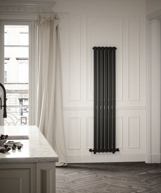 dark grey vertical radiator hung on panelled wall in kitchen with white walls and wooden floor