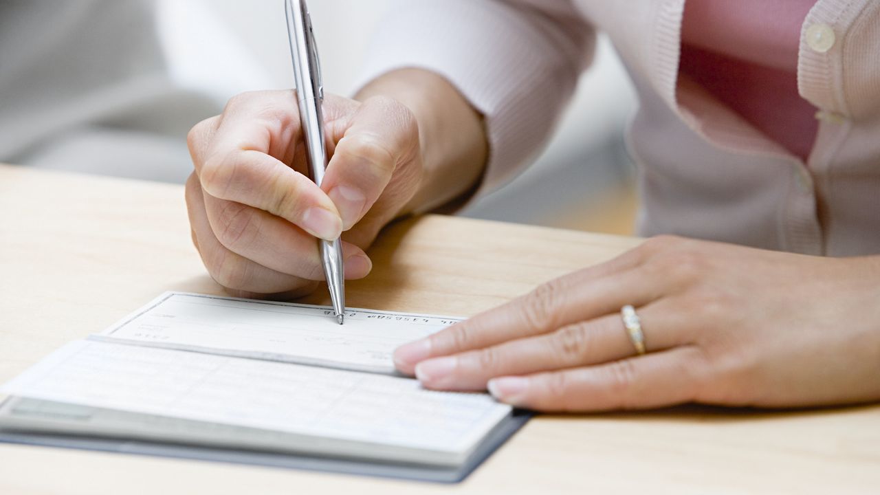 A woman writes out a check, only her hands and the checkbook showing.