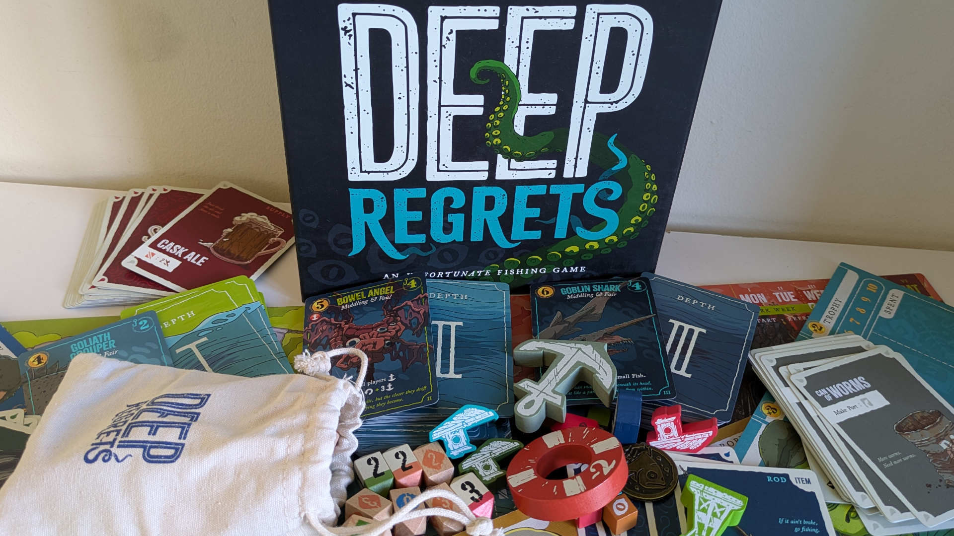Deep Regrets box and contents on a white wooden surface
