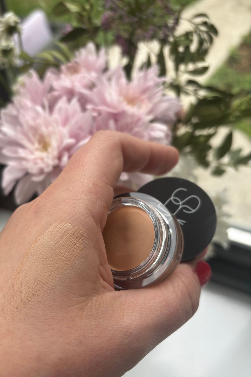 a hand holding a pot of nars concealer with a smear of product
