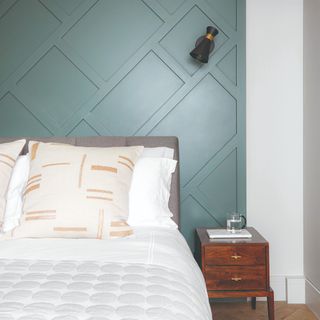 A bedroom with a panelled duck egg-painted wall behind the bed