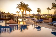 Wyndham Residences, Costa Del Sol. Image of the lagoon pool with blue sun loungers at sunset 