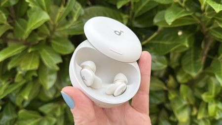 A hand holding the Soundcore Sleep A30 earbuds against a green hedge.
