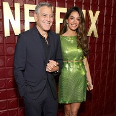 Amal Clooney walks on the red carpet with George Clooney wearing a green Versace dress with gold and vinyl heels.