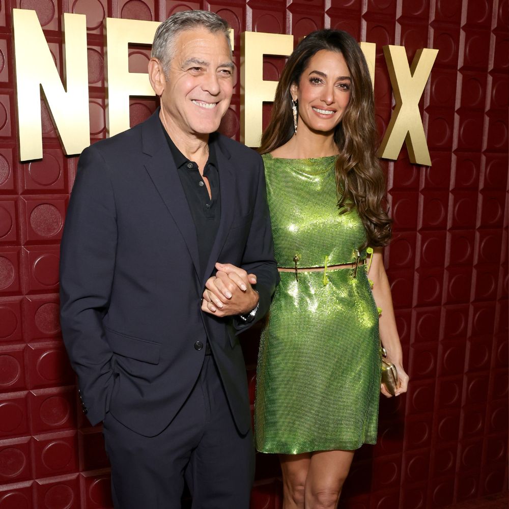 Amal Clooney walks on the red carpet with George Clooney wearing a green Versace dress with gold and vinyl heels.