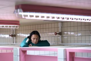 A man (Roh Jae-won) rests his elbows on the top of a pink-and-white bathroom stall, in 'Squid Game' season 2.