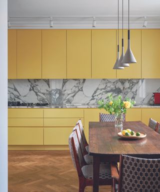 Yellow kitchen cabinets with a marble back splash and a wooden dining table