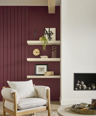 living room with white wall and burgundy accent wall, neutral armchair and open shelving