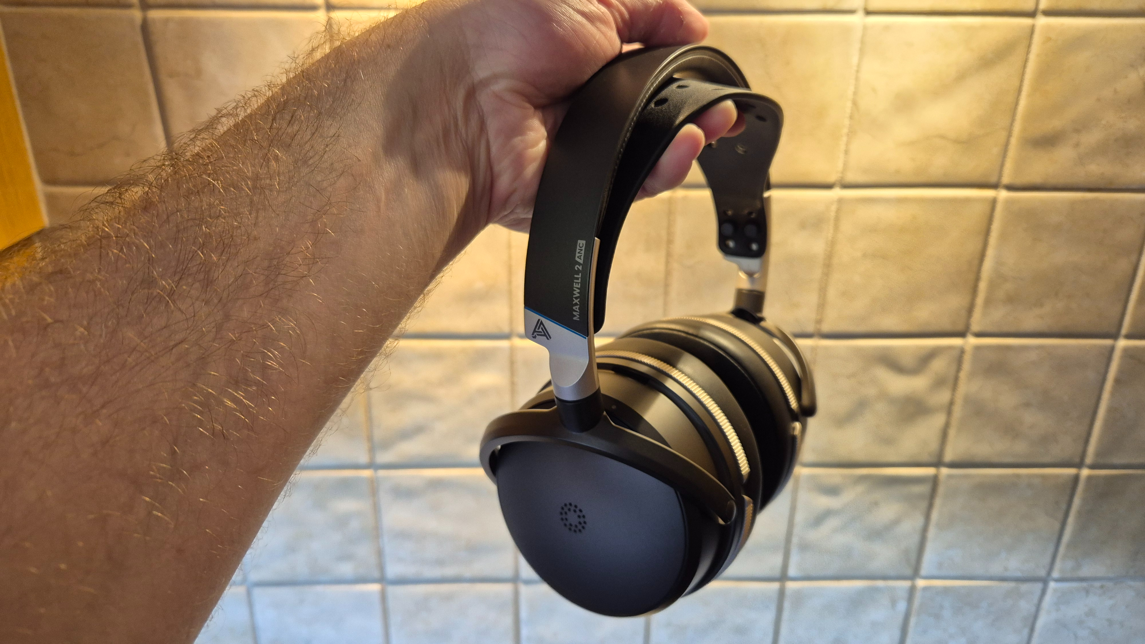 A picture of the Audeze Maxwell 2 ANC gaming headset being held in a hand with pale tiles in the background