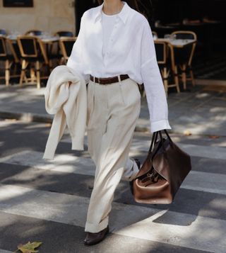 woman crossing the road wearing cream tailoring and carrying a brown row margaux bag