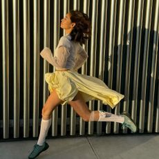 Influencer @himichelleli jumps through the air wearing green Keen trainers with a white skirt and grey top.