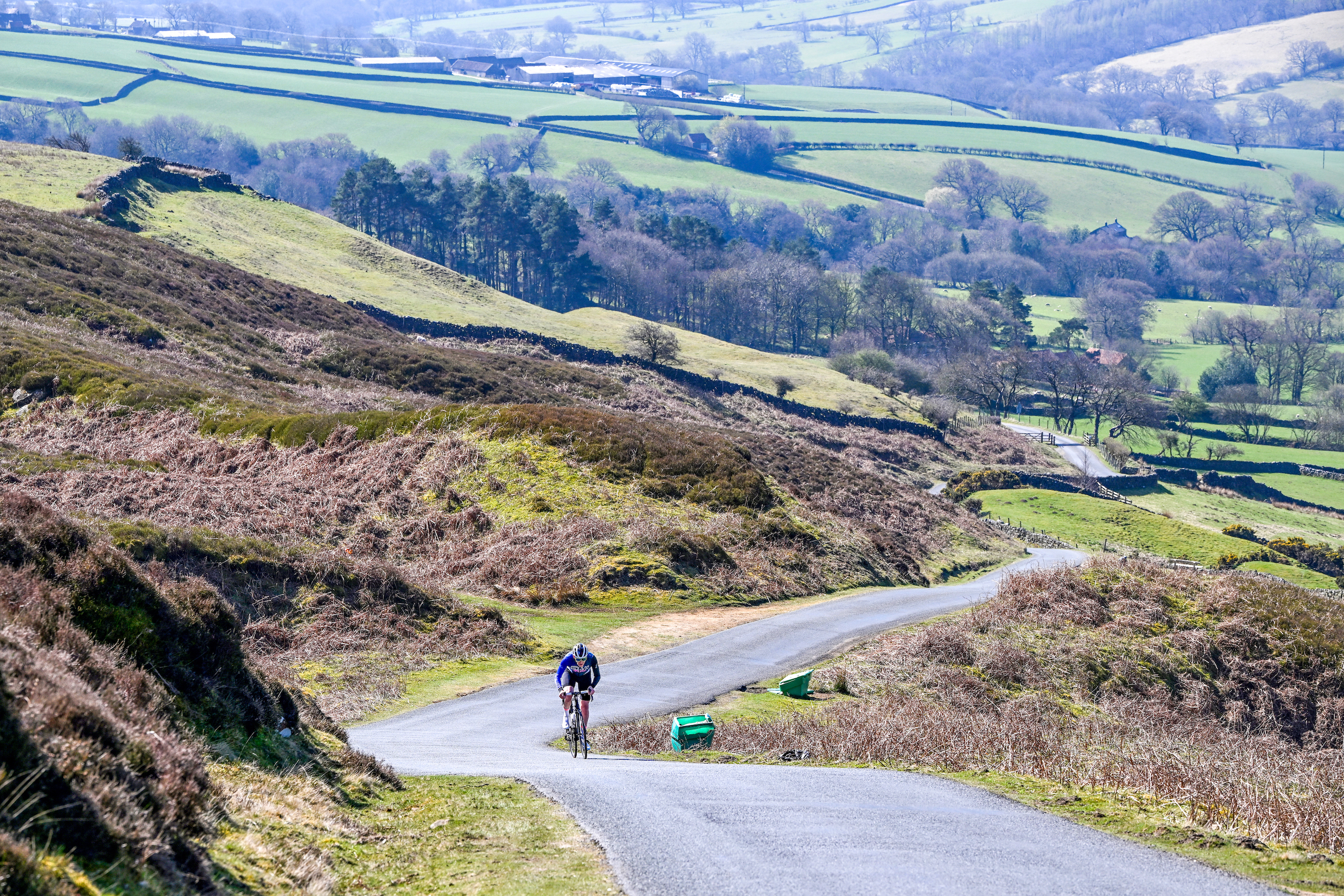In the distance, a male rider in blue kit is climbing towards us, the road snaking away behind him amid North York Moors scenery