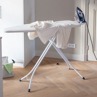 ironing board with a sheet and iron in a kitchen with herringbone wood floor