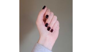 A close-up picture of Digital Beauty Writer, Naomi Jamieson's hand with dark plum squoval nails, against a green backdrop