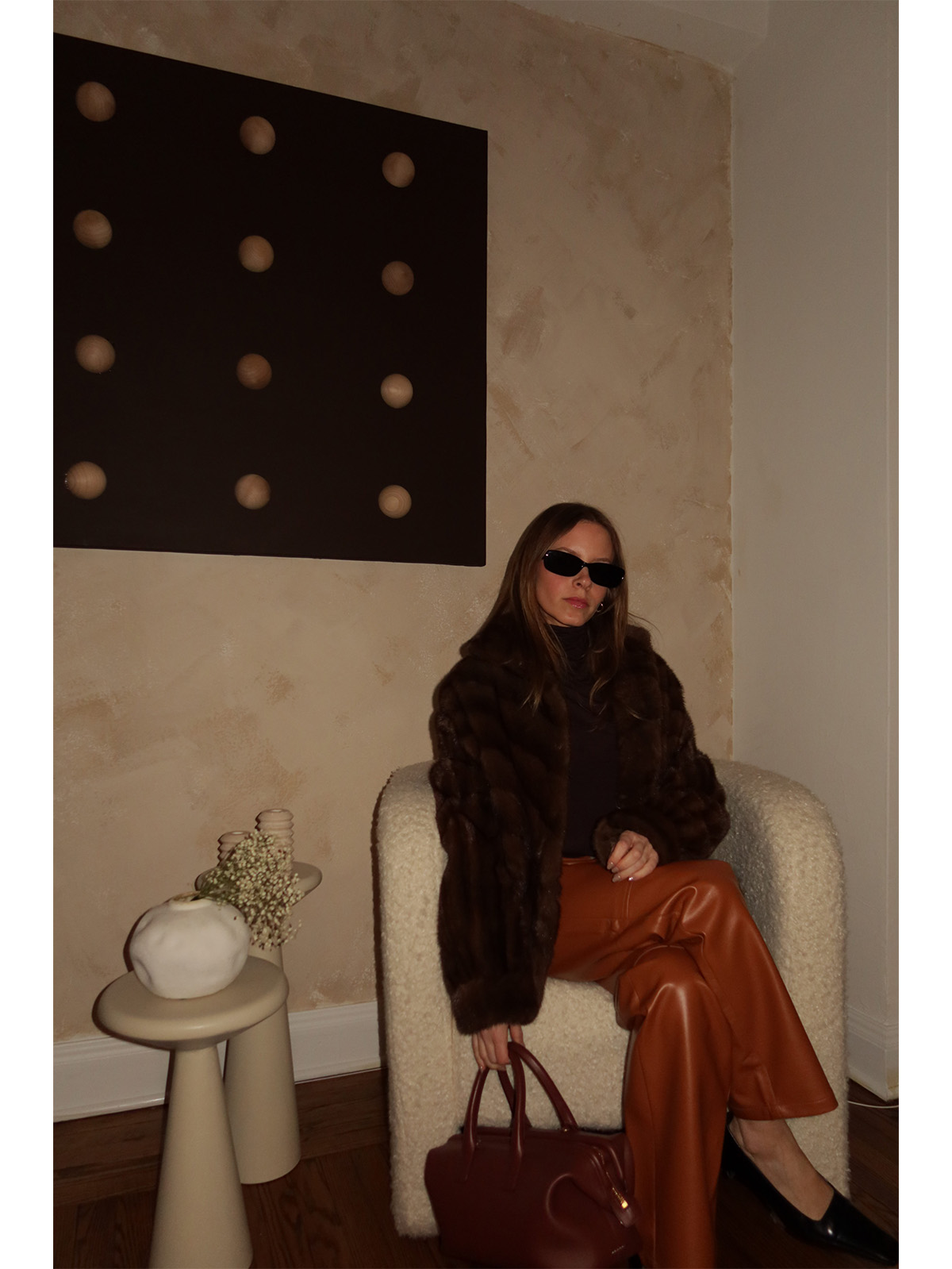 Nikki wears a fur coat, brown cashmere heattech shirt, leather pants, and black pumps.