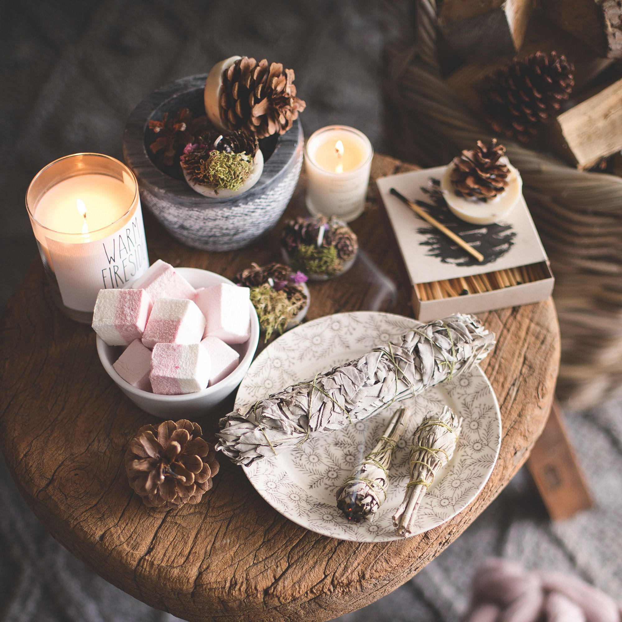 A wooden side table with candles and a sage bundle on top