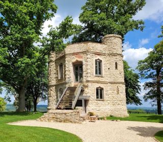 Dinton Castle has white stone work for its structure as well as stairs leading up to its entrance which follows on from the gravelled driveway. It is surrounded by greenery and trees in a secluded area