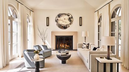 living room with high ceiling and fire lit pale cream sofa and blue armchairs and round artwork above mantel
