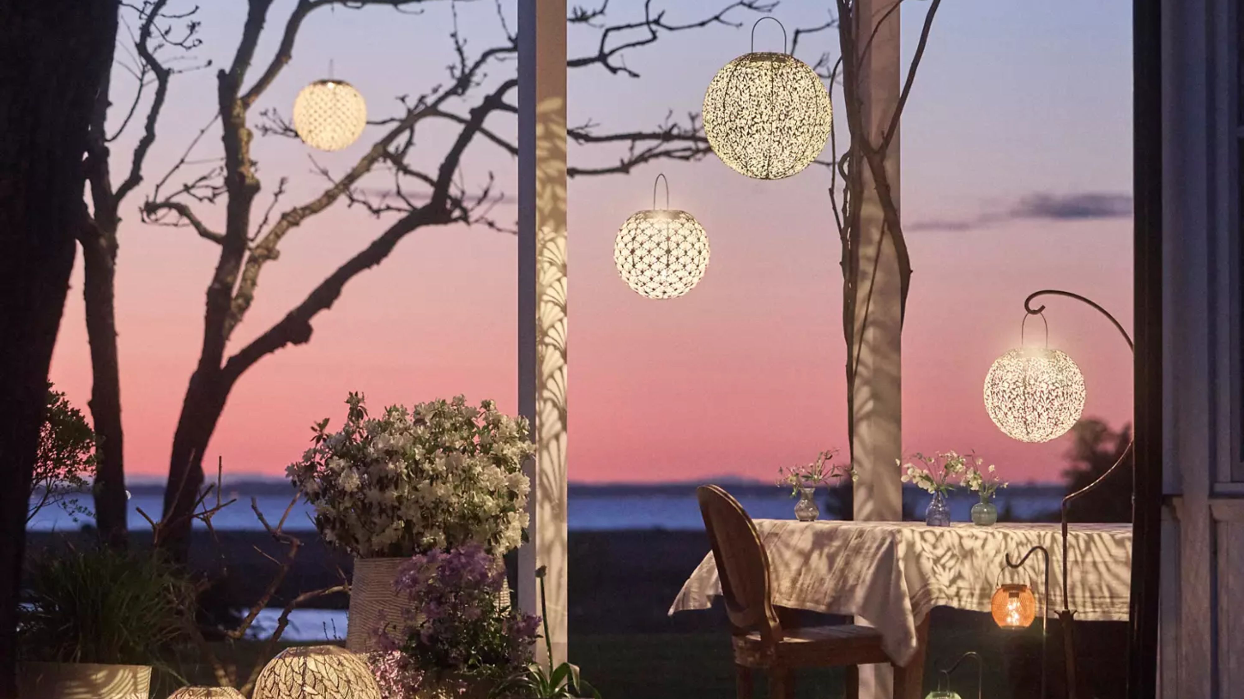 Enchanting outdoor patio at sunset featuring a dining table and several etched-metal, Art Nouveau-inspired solar lights