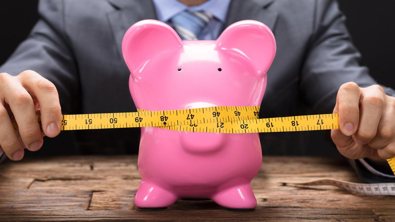 A piggy bank being squeezed by a measuring tape.