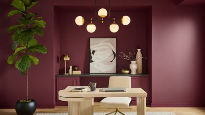 modern home office with win red walls, light wooden desk, large houseplant and mid-century modern pendant light