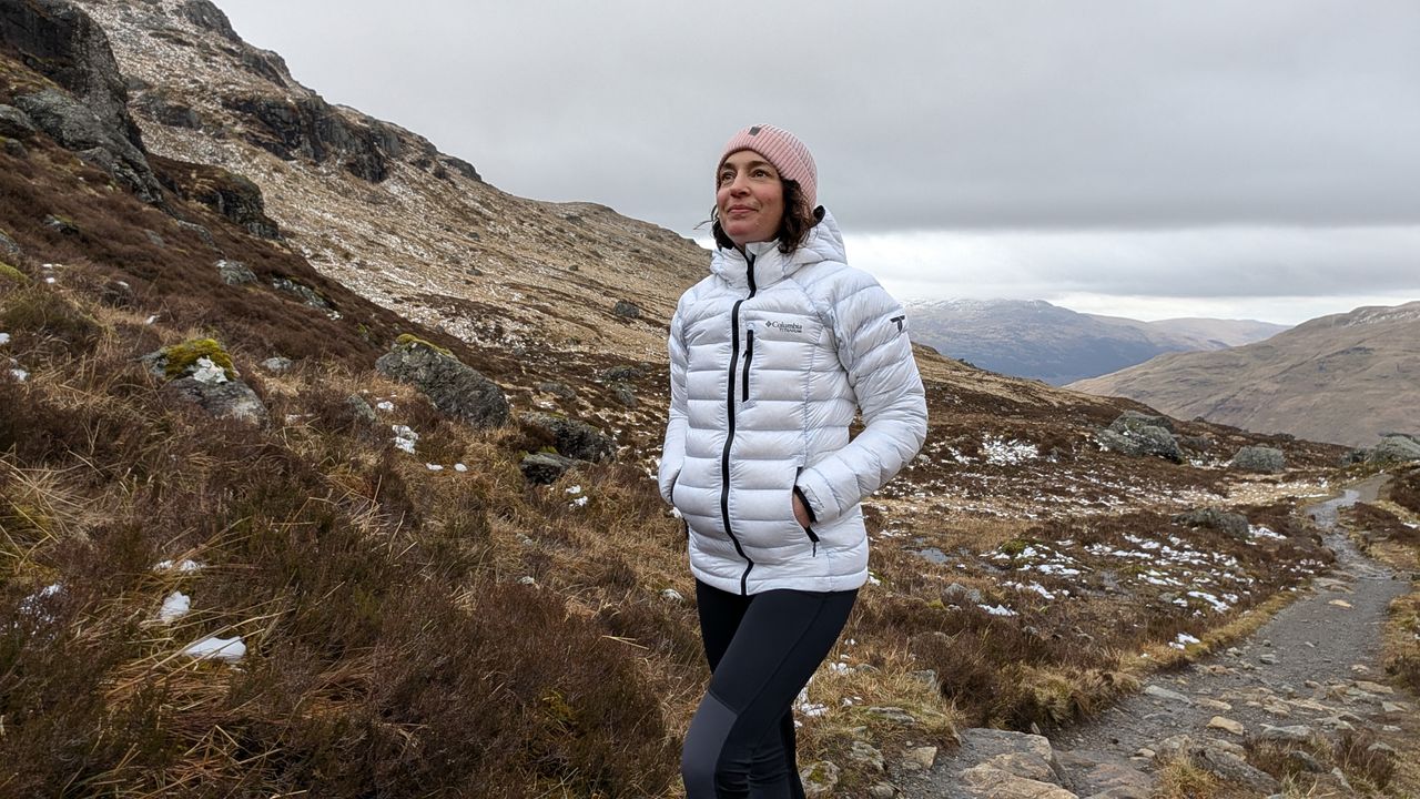 A woman hiking in the mountains wearing a white Columbia Arctic Crest Down jacket