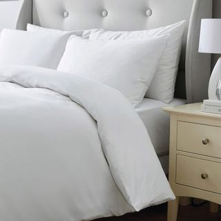 A close up of a bed with white bedlinen and a wooden side table