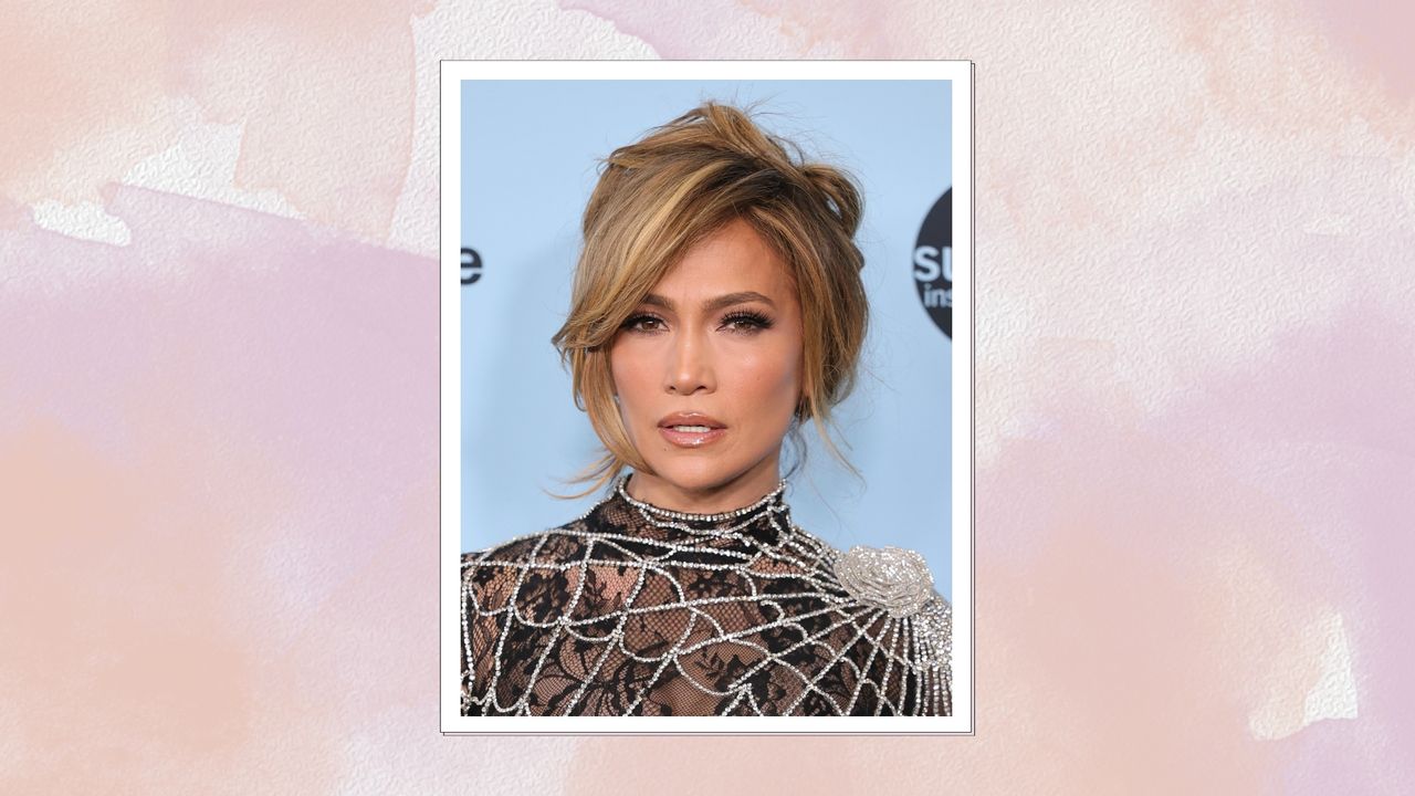 Image of Jennifer Lopez with a brunette updo and wearing a spiderweb black lace gown, on a pink watercolour background