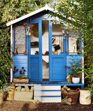 blue coloured garden shed with potted plant and wood storage basket