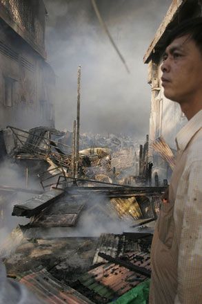 A photo taken past a man towards a demolished, smoking landscape