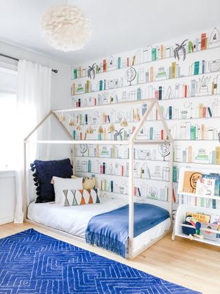 boys bedroom with bookcase wallpaper, house frame bed, blue rug, wooden floorboards