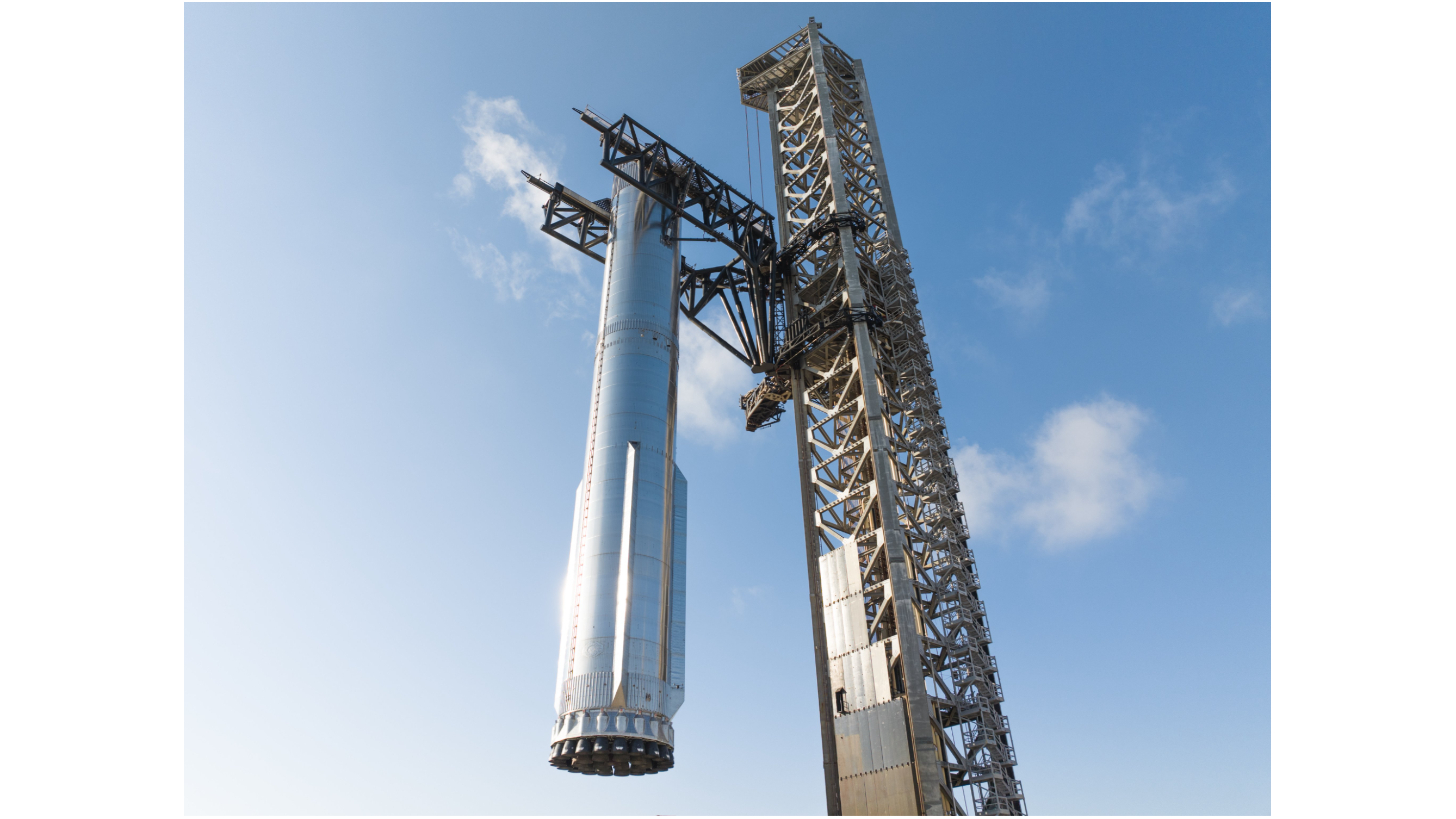 closeup of a large silver rocket being hoisted by the arms of its metallic launch tower