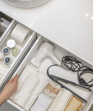 An image of a bathroom drawer open by a sink with storage trays and products neatly organized