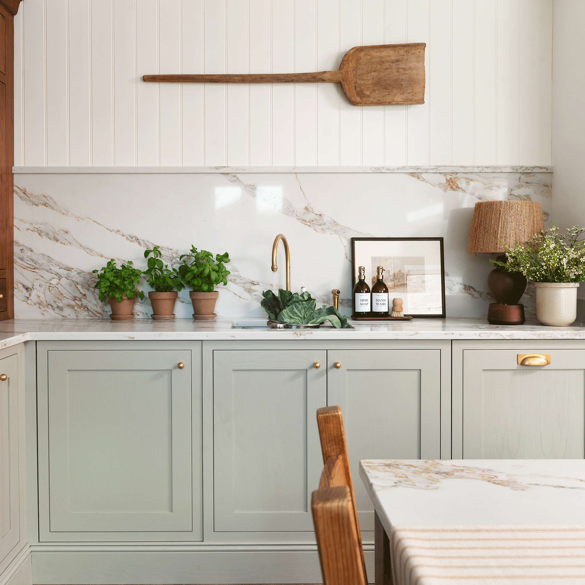 a neutral country-style kitchen with pale green cabinetry and a marble splashback