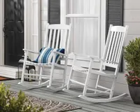 A pair of white rocking chairs on a front porch with shuttered windows behind