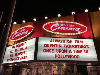 An Art Deco cinema facade is illuminated with warm lights. Its sign reads: Beverly Cinema. Always on film Quentin Tarantino's Once Upon a Time in... Hollywood.