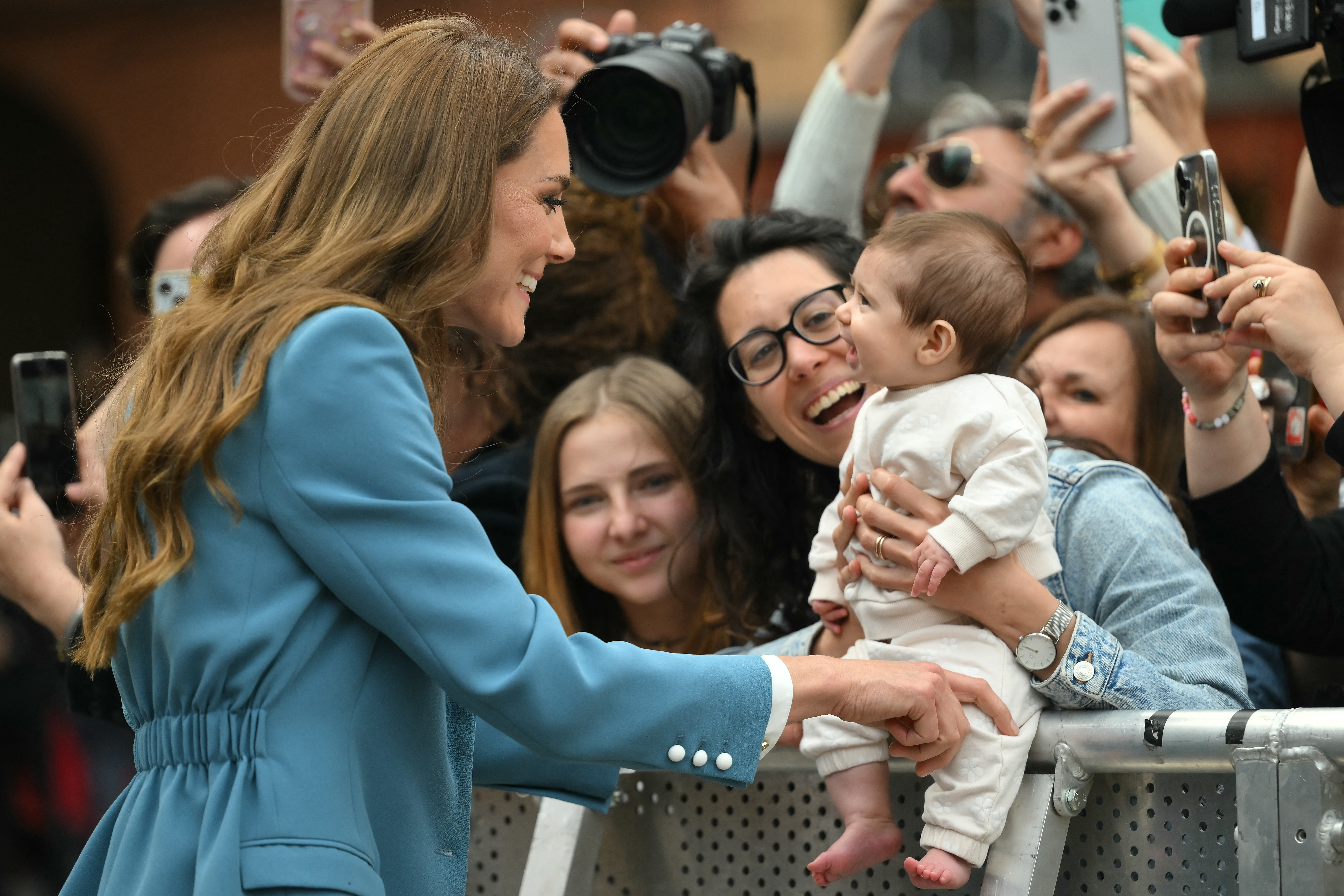 Princess Kate wearing a blue suit smiling at a baby