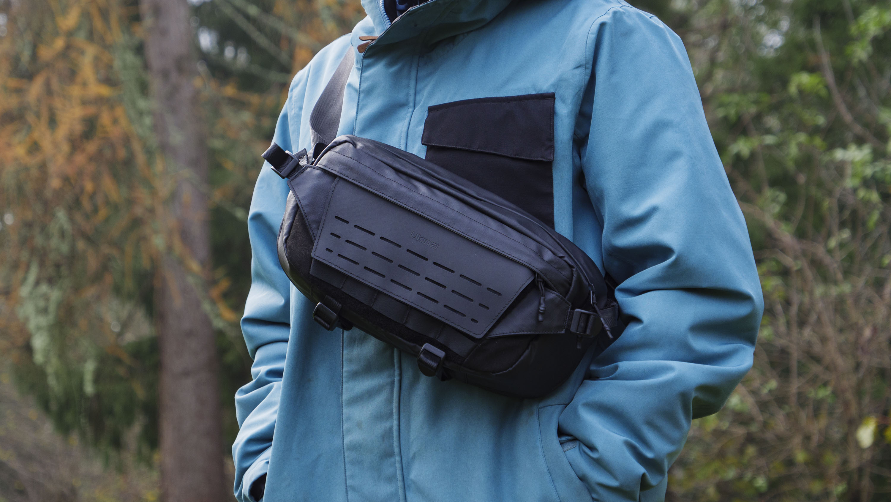 Man wearing a blue jacket outside with a Ulanzi Camera Sling Bag over his shoulder and resting on his midriff
