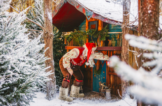 Father Christmas in the snow peeking into a log cabin at Lapland UK