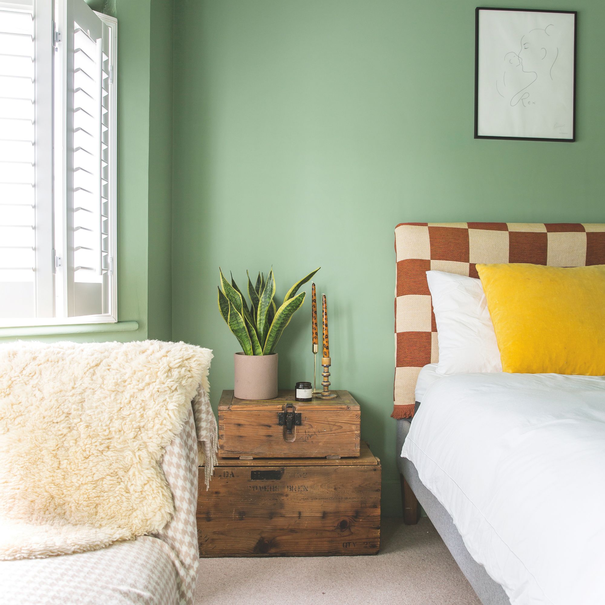 Green painted bedroom with a white bed and a checkerboard headboard, with storage trunks next to it