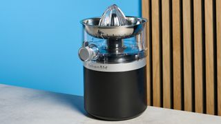 KitchenAid Go Cordless Citrus Juicer in matte black photographed in front of a blue background.