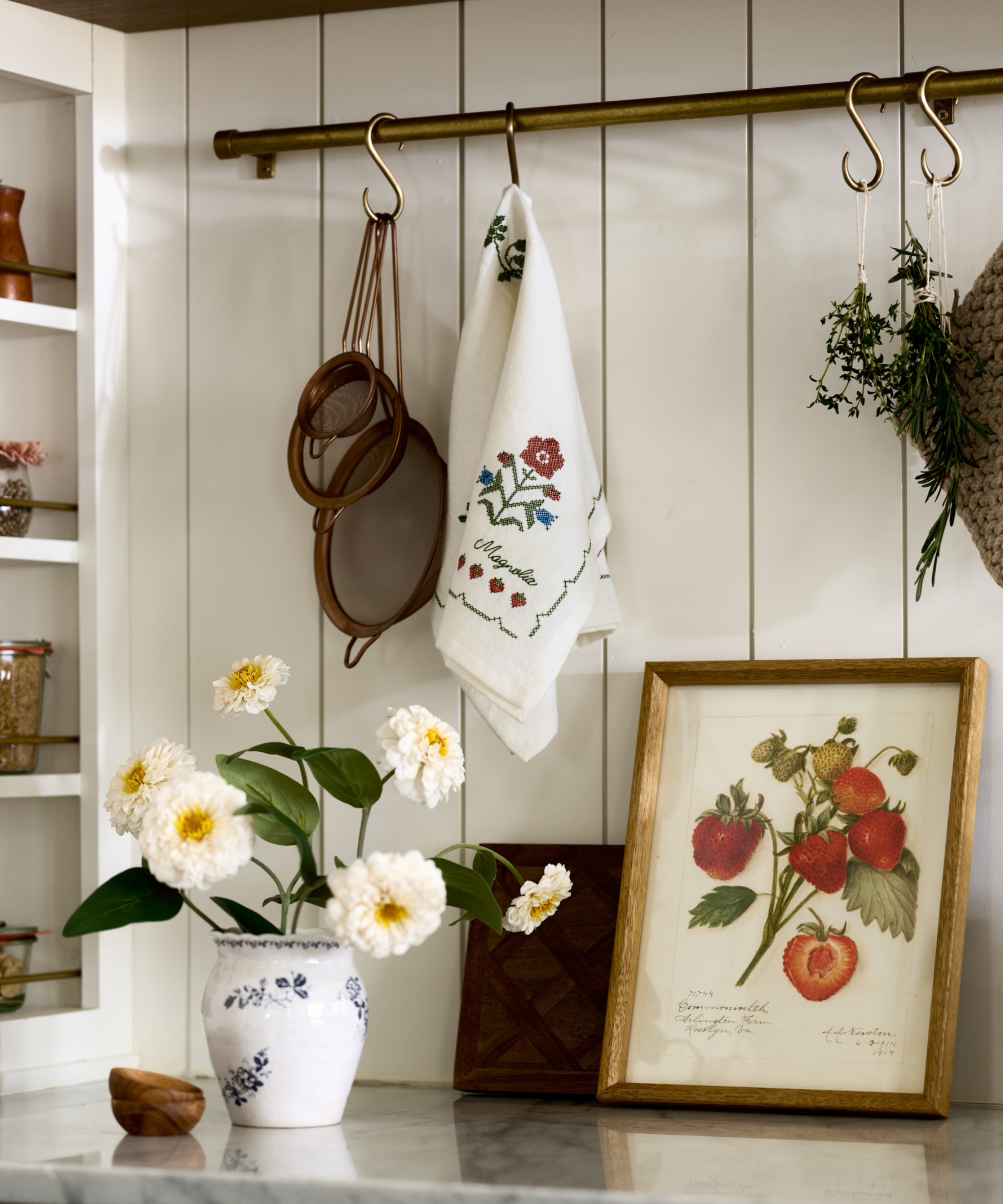 a kitchen countertop with artwork, a vase of flowers, and a pot rack with kitchen necessities hanging